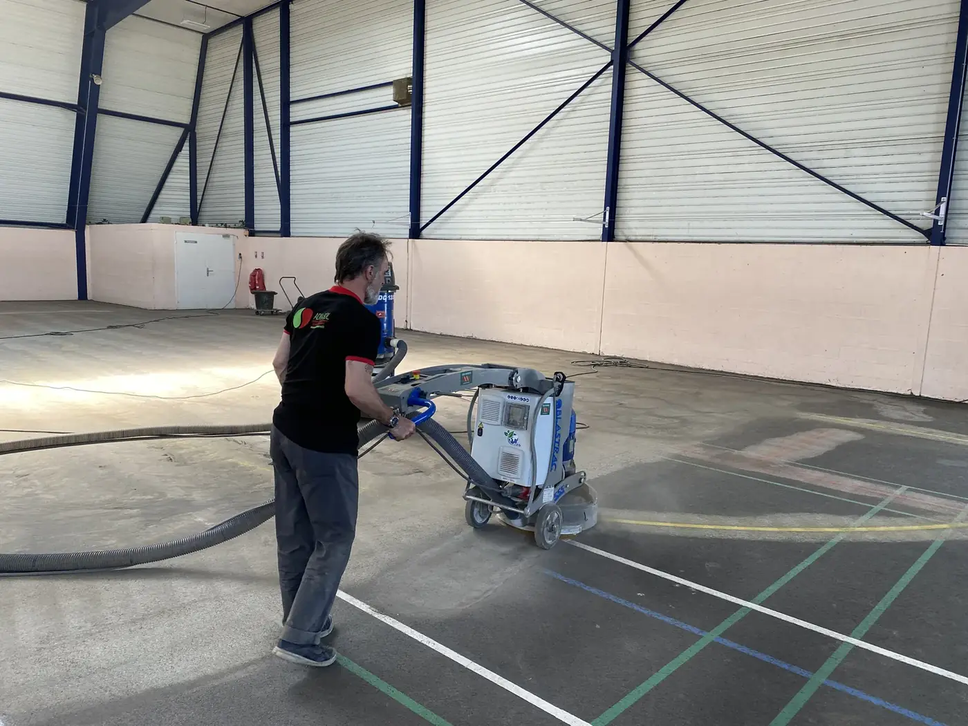 Technicien ADN-SOL en phase de ponçage et préparation du support avant rénovation du sol sportif